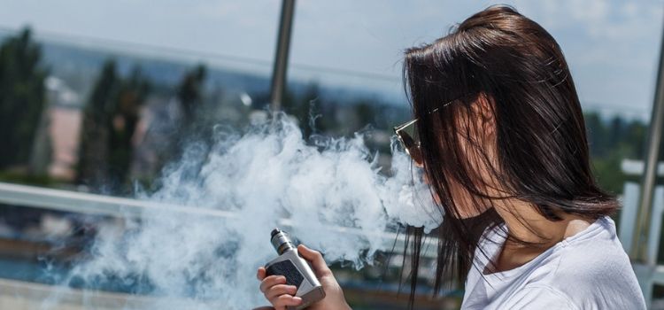 A young woman smokes a JUUL e-cigarette
